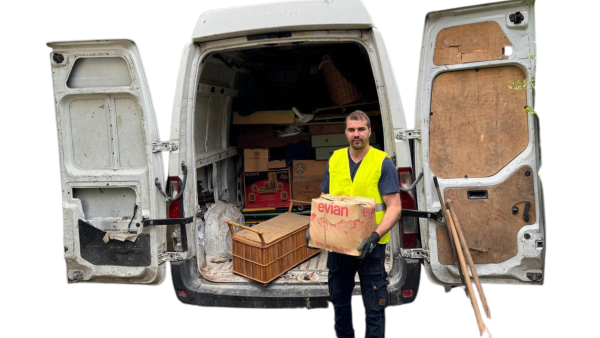 Un employé de DND Services vidant un camion de débarras, portant un carton devant un véhicule utilitaire rempli de divers objets à débarrasser en Île-de-France.